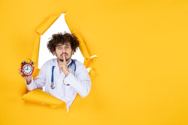 Vue de face médecin de sexe masculin en costume médical tenant des horloges sur l'hôpital jaune shopping couleur médecine temps medic