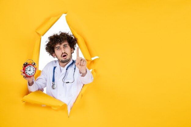 Vue de face médecin de sexe masculin en costume médical tenant des horloges sur l'hôpital jaune shopping médecine couleur temps santé