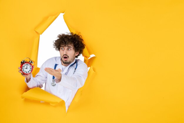Vue de face médecin de sexe masculin en costume médical tenant des horloges sur le virus de l'hôpital de temps de santé médical de couleur jaune