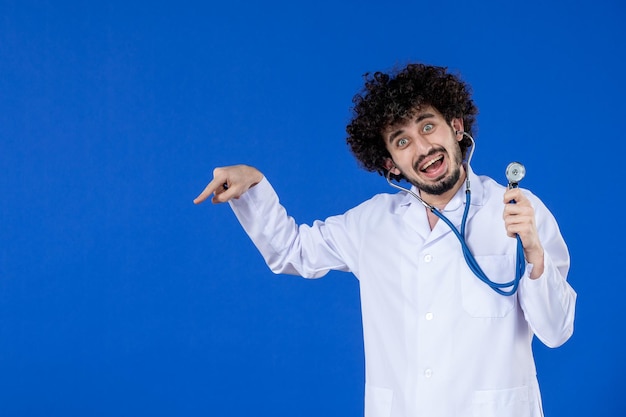 Vue de face d'un médecin de sexe masculin excité en costume médical avec stéthoscope sur une surface bleue