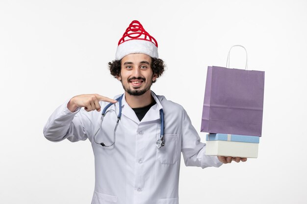 Vue de face d'un médecin de sexe masculin tenant des cadeaux sur un mur blanc