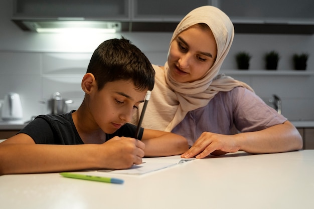 Vue de face mère aidant un enfant à faire ses devoirs