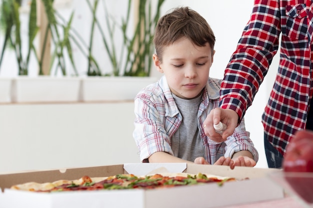 Vue de face de la mère désinfectant les mains de son fils avant de manger une pizza