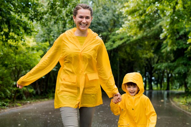 Vue de face mère et fils se tenant la main tout en portant des manteaux de pluie