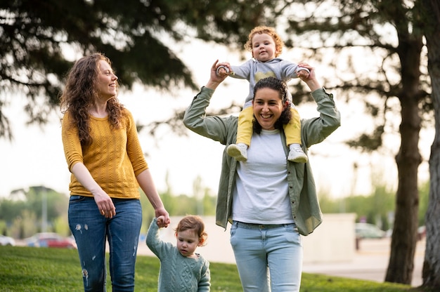 Vue de face des mères lgbt smiley à l'extérieur dans le parc avec leurs enfants