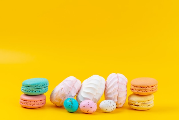 Une vue de face meringues et macarons délicieux et sucrés sur des bonbons arc-en-ciel de couleur jaune