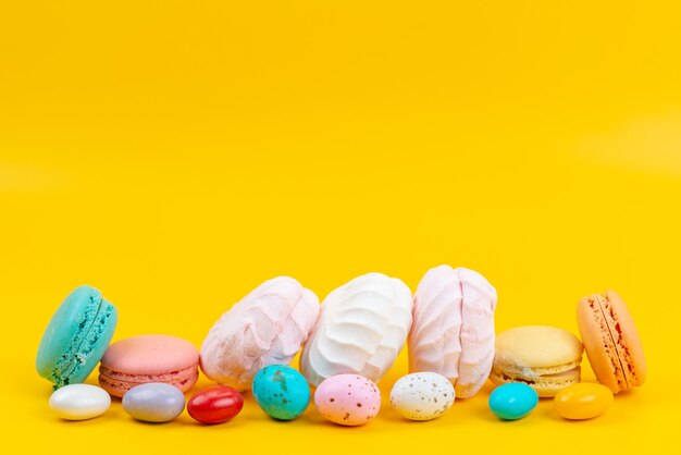 Une vue de face meringues et macarons délicieux et sucrés sur des bonbons arc-en-ciel de couleur jaune
