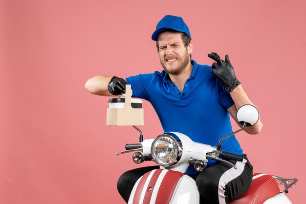 Vue de face messager masculin en uniforme bleu tenant un café sur un travail de couleur de travailleur de vélo de livraison de restauration rapide rose