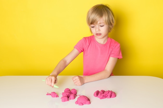 Une vue de face mignon adorable garçon en t-shirt rose jouant avec du sable cinétique coloré