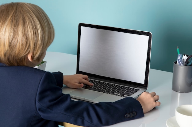 Une vue de face mignon garçon d'affaires en costume classique bleu en face de l'ordinateur portable argenté mode de travail d'entreprise