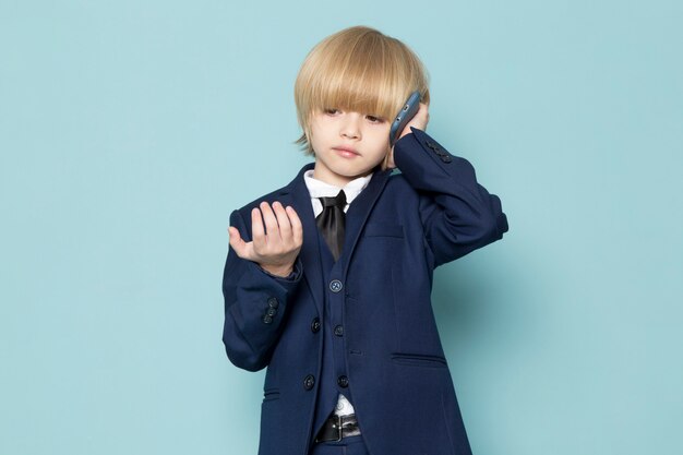 Une vue de face mignon garçon d'affaires en costume classique bleu posant parler au téléphone