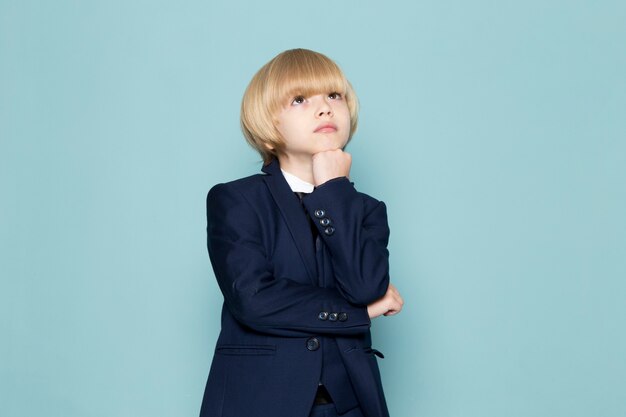 Une vue de face mignon garçon d'affaires en costume classique bleu posant la rêverie en pensant à la mode de travail d'entreprise