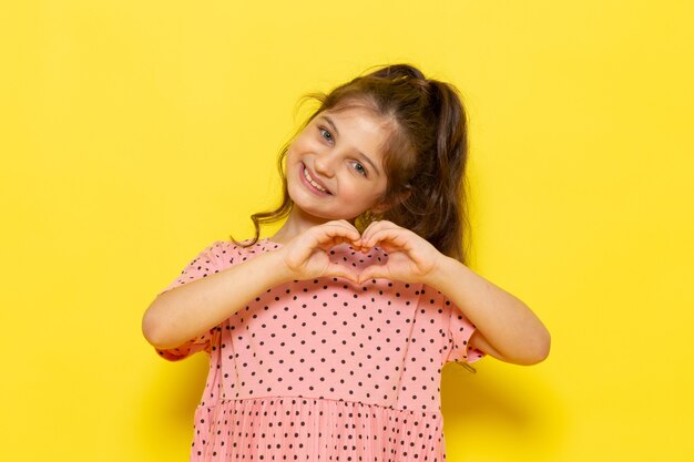 Une vue de face mignon petit enfant en robe rose souriant et montrant un signe d'amour