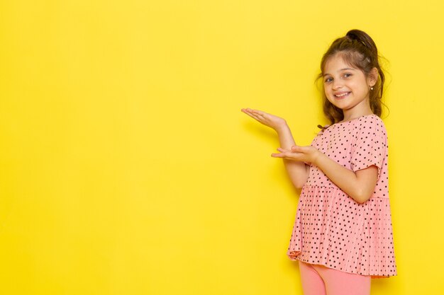 Une vue de face mignon petit enfant en robe rose souriant et posant