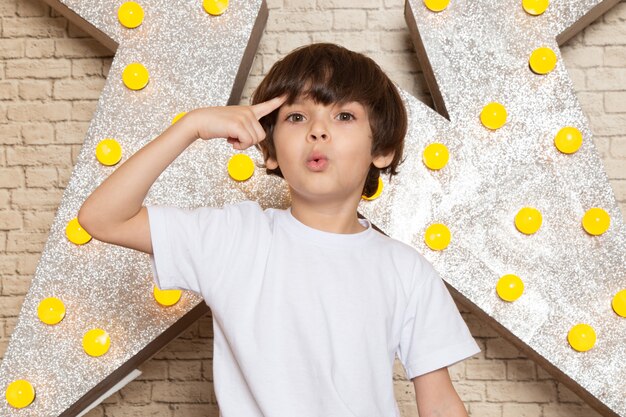 Une vue de face mignon petit enfant en t-shirt blanc jean foncé sur l'étoile conçu stand jaune et fond clair