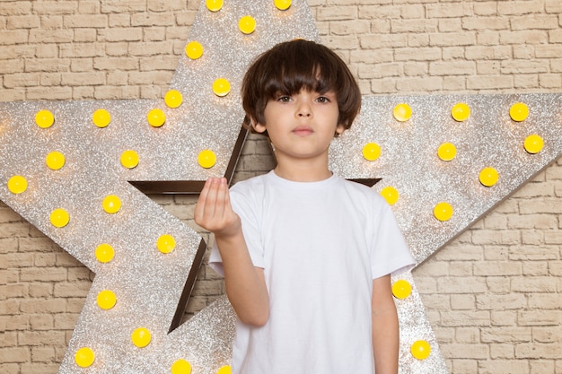 Une vue de face mignon petit enfant en t-shirt blanc jean foncé sur l'étoile conçu stand jaune et fond clair