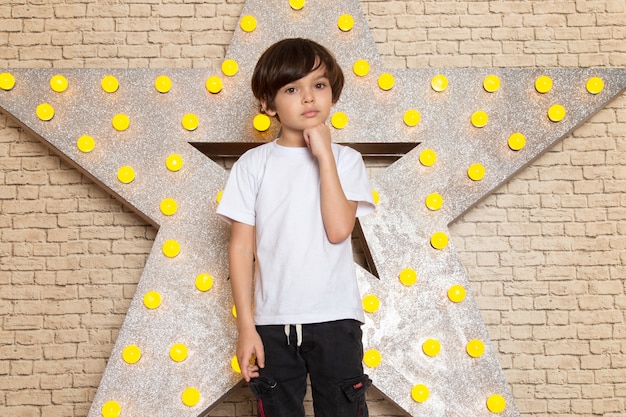 Photo gratuite une vue de face mignon petit enfant en t-shirt blanc jean foncé sur l'étoile conçu stand jaune et fond clair