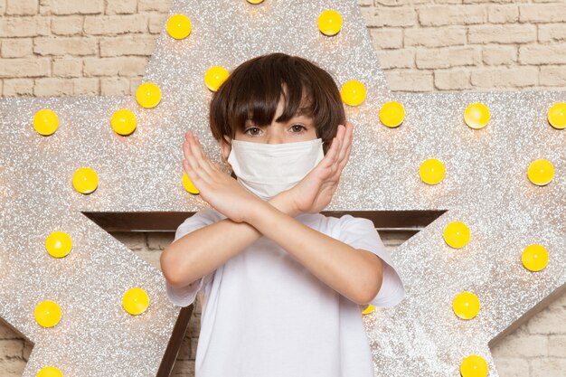 Une vue de face mignon petit enfant en t-shirt blanc jean foncé masque stérile blanc sur l'étoile conçu stand jaune et fond clair