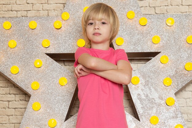 Une vue de face mignon petit enfant en t-shirt rose jeans gris sur l'étoile conçu stand jaune et fond clair