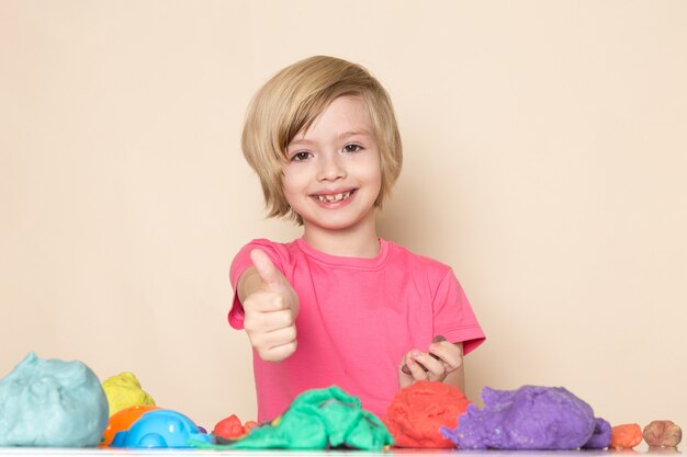 Une vue de face mignon petit enfant en t-shirt rose montrant un signe impressionnant jouant avec du sable cinétique coloré