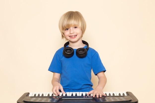 Une vue de face mignon petit garçon souriant en t-shirt bleu avec un casque noir jouant un petit piano mignon