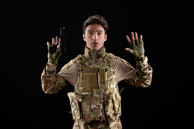 Vue de face d'un militaire en uniforme se rendant avec une arme à feu sur un mur noir