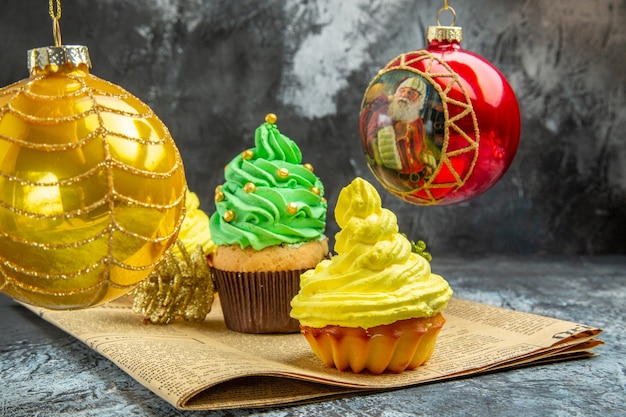 Vue de face mini cupcakes colorés boules d'arbres de Noël rouges sur journal sur photo sombre du nouvel an