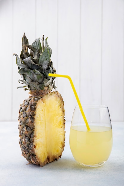 Vue de face de la moitié de l'ananas et verre de jus d'ananas avec tube à boire sur une surface blanche