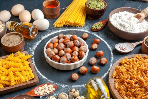 Vue de face noisettes fraîches avec des oeufs d'huile de pâtes crues et de la farine sur fond sombre cuire la pâte photo repas cuisine couleur