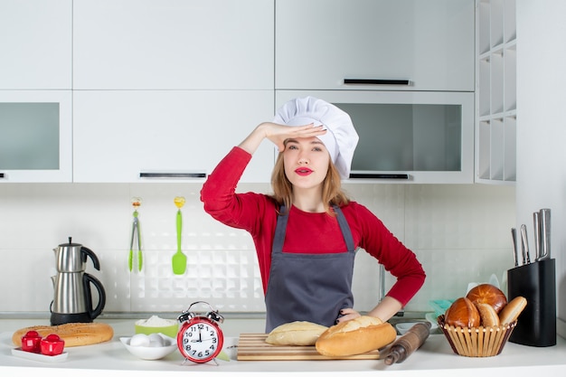 Vue de face observant la jeune femme en chapeau de cuisinier et tablier dans la cuisine