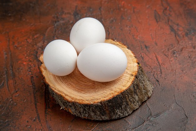 Vue de face des œufs de poule blancs sur bois sur une surface sombre