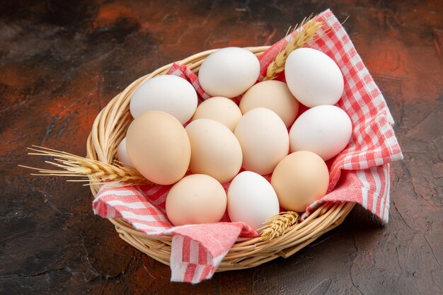 Vue de face des œufs de poule blancs à l'intérieur du panier avec une serviette sur la surface sombre