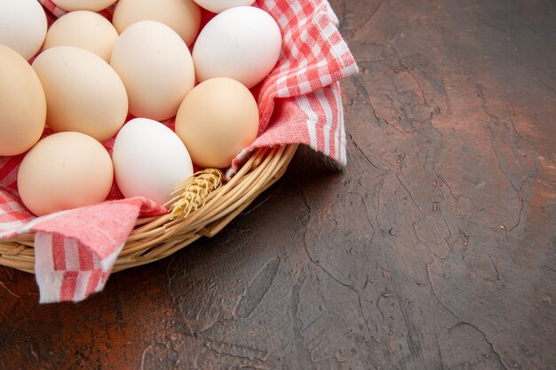 Vue de face des œufs de poule blancs à l'intérieur du panier avec une serviette sur la surface sombre