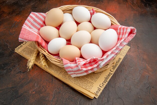 Vue de face des œufs de poule blancs à l'intérieur du panier avec une serviette sur la surface sombre