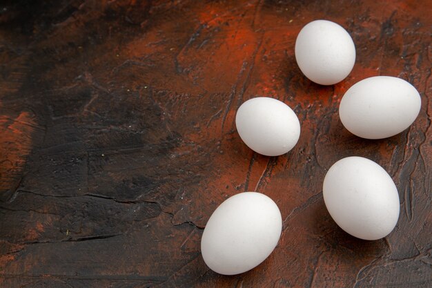 Vue de face des œufs de poule blancs sur la surface sombre