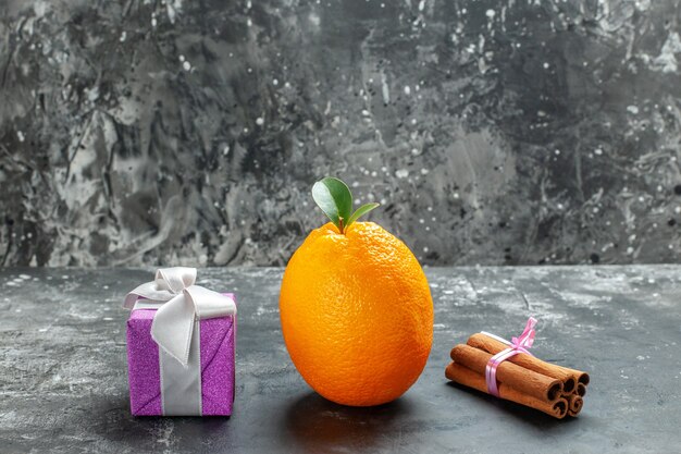 Vue de face d'orange fraîche biologique avec tige et feuille près d'un cadeau et citrons verts à la cannelle sur fond sombre