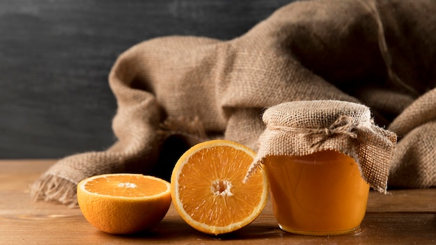 Vue de face des oranges et du pot de marmelade et de la toile de jute