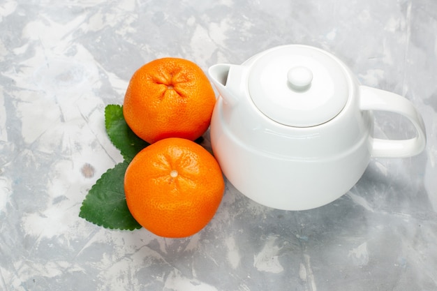 Vue de face des oranges fraîches avec bouilloire sur surface blanche