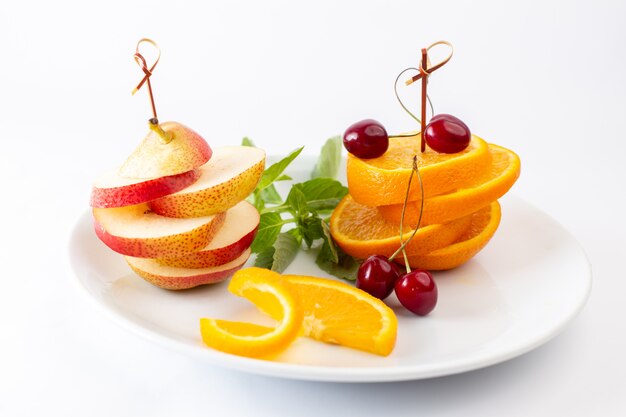 Vue de face oranges fraîches tranchées à l'intérieur de la plaque blanche avec cerises rouges et poire sur blanc