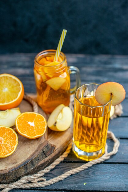 Vue de face des oranges et des pommes coupées en cocktail sur planche de bois sur fond isolé sombre