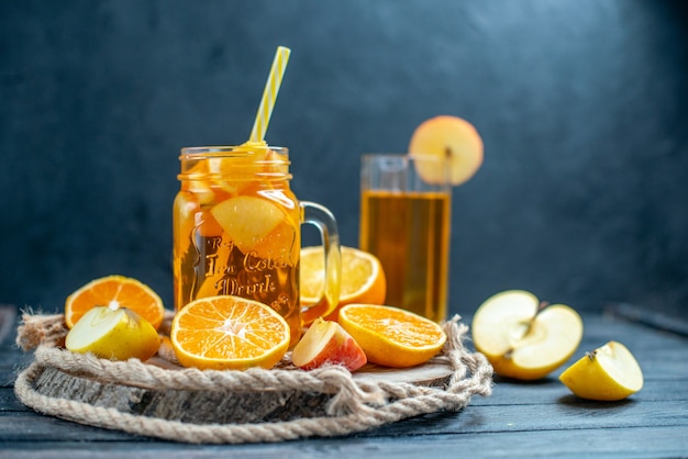 Vue de face des oranges et des pommes coupées en cocktail sur planche de bois sur fond isolé sombre