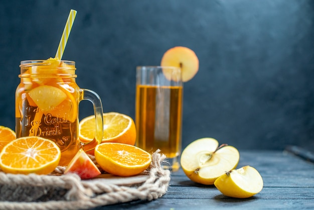 Photo gratuite vue de face des oranges et des pommes coupées en cocktail sur planche de bois sur fond isolé sombre