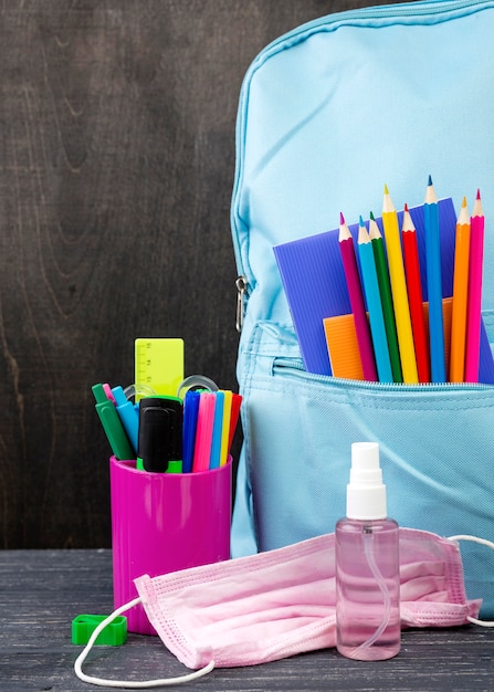 Vue de face de la papeterie de retour à l'école avec masque médical et désinfectant pour les mains