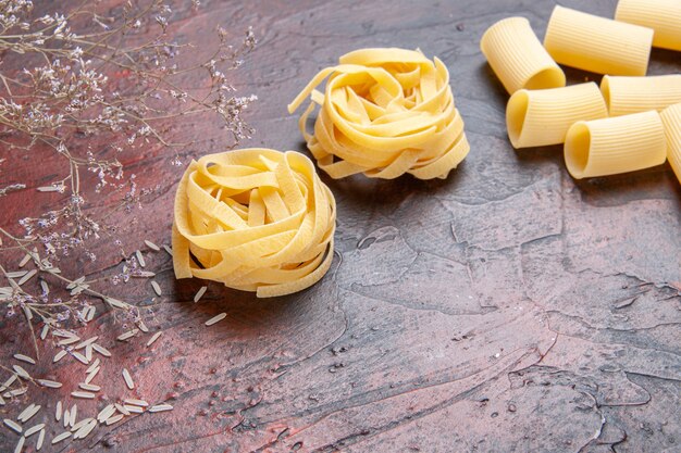 Vue de face des pâtes crues sur des pâtes de couleur pâte à surface foncée