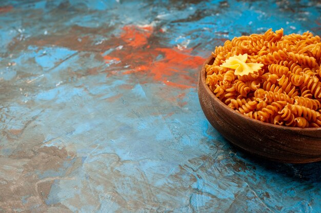 Vue de face des pâtes italiennes crues dans un bol marron sur une table bleue