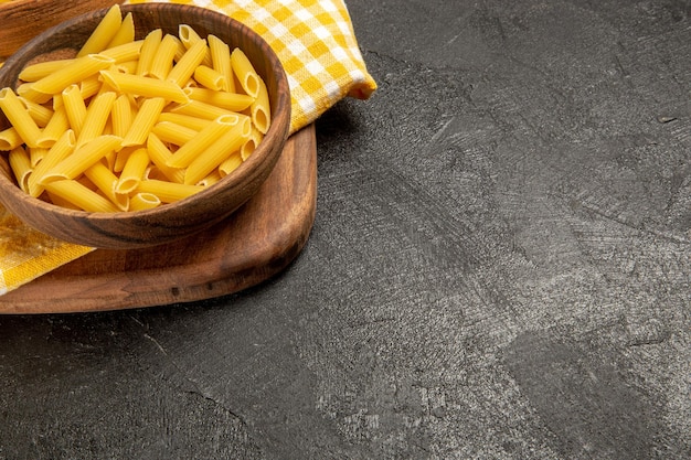 Vue de face des pâtes italiennes crues à l'intérieur d'assiettes brunes sur un espace gris foncé