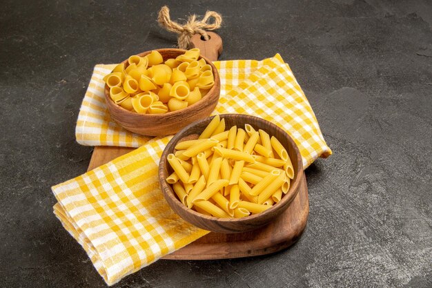 Vue de face des pâtes italiennes crues à l'intérieur d'assiettes brunes sur un espace gris