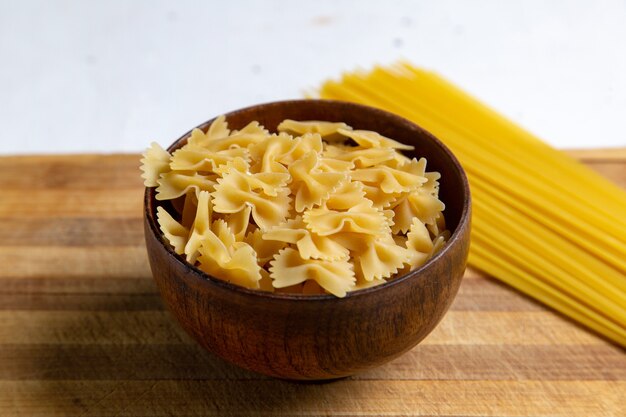 Une vue de face des pâtes italiennes crues peu formé à l'intérieur de la plaque brune sur la table en bois de pâtes italiennes repas