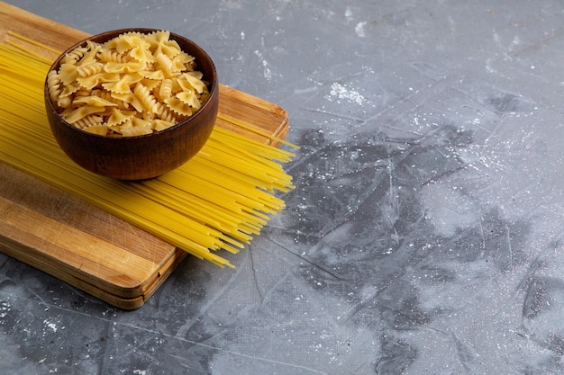 Une vue de face des pâtes italiennes crues peu et longtemps formé à l'intérieur de la plaque brune sur la table grise des pâtes italiennes repas