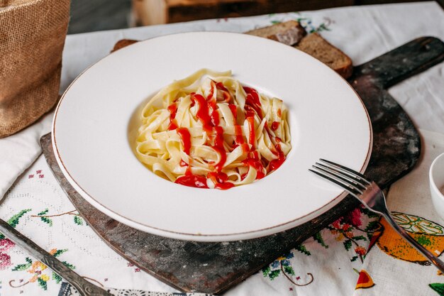 Une vue de face des pâtes avec sauce tomate rouge poivrée salée à l'intérieur de la plaque blanche repas de pâte italienne sur le bureau brun